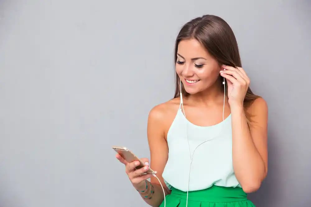 Smiling young girl listening music on smartphone over gray background_11zon