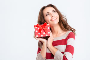 Portrait of a happy thoughtful woman holding gift box and looking up isolated on a white background