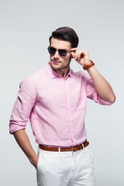 Portrait of a trendy young man in sunglasses and pink shirt over gray background-1