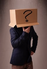 Young man standing and gesturing with a cardboard box on his head with question mark